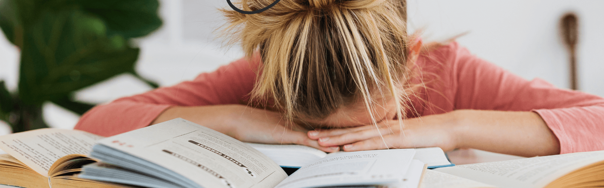 Frau mit Burnout liegt mit dem Kopf auf dem Tisch mit Büchern.