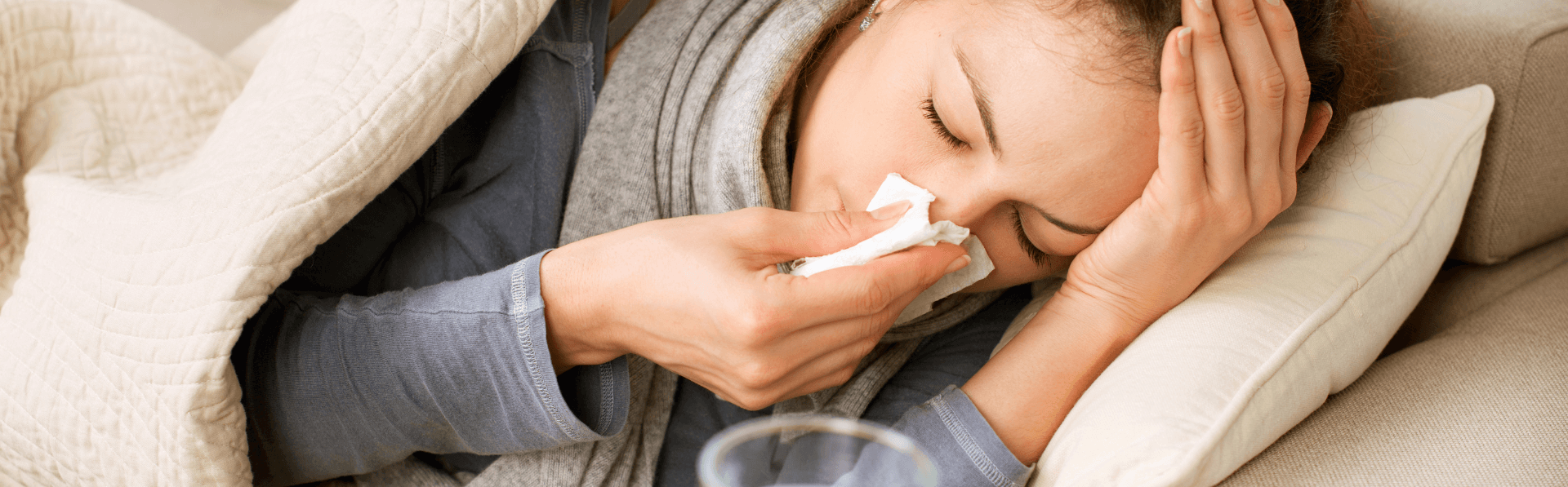Frau ist ständig krank und liegt mit Erkältung und Taschentuch auf dem Sofa.