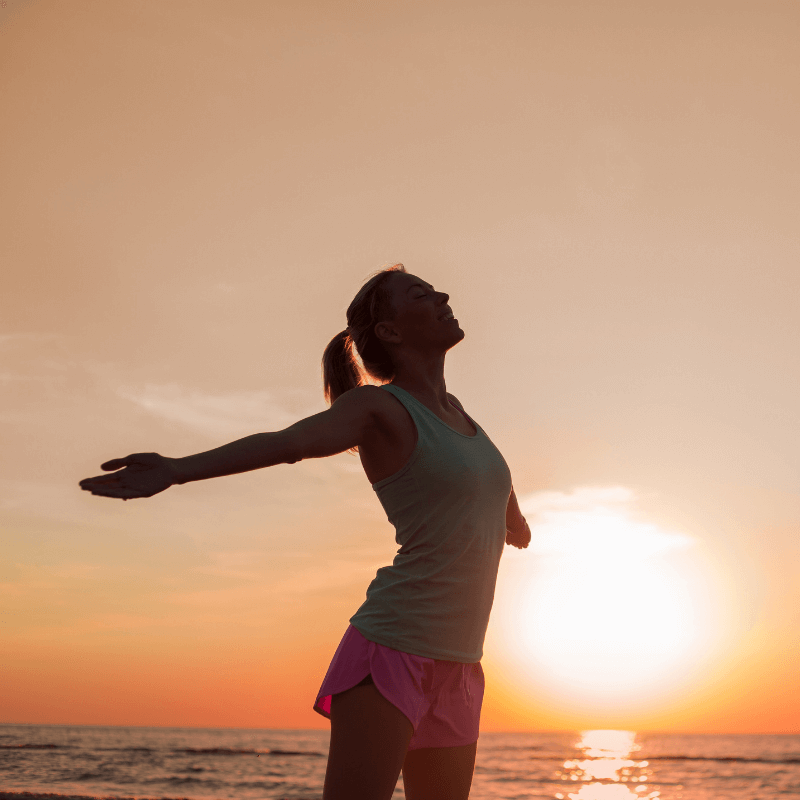 Frau streckt beide Arme weit von sich und atmet tief ein als Teil ihrer Longevity-Maßahmen.