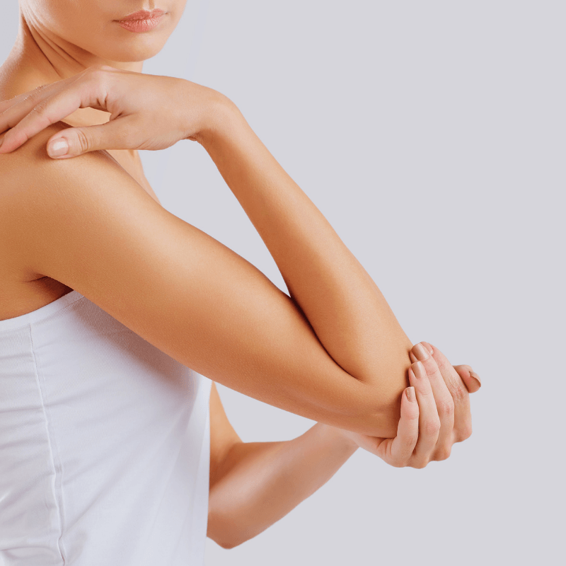 Frau mit Rheuma greift sich mit einer Hand an ihren Ellenbogen.