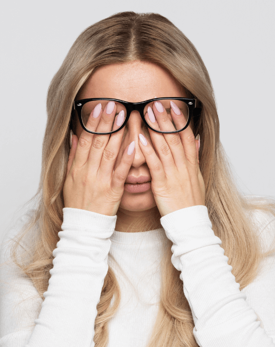 Frau hält sich Augen zu aufgrund von Kopfschmerzen und Erschöpfung bei Long Covid.