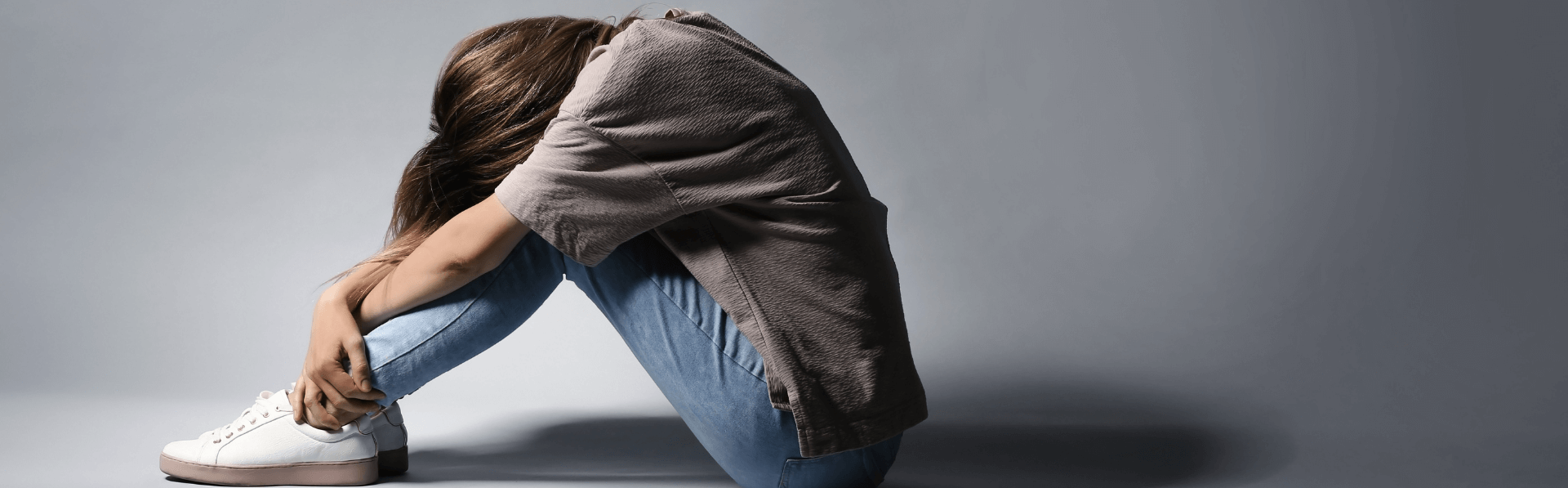 Frau die an einer Depression leidet sitzt mit gesenktem Kopf auf dem Boden.
