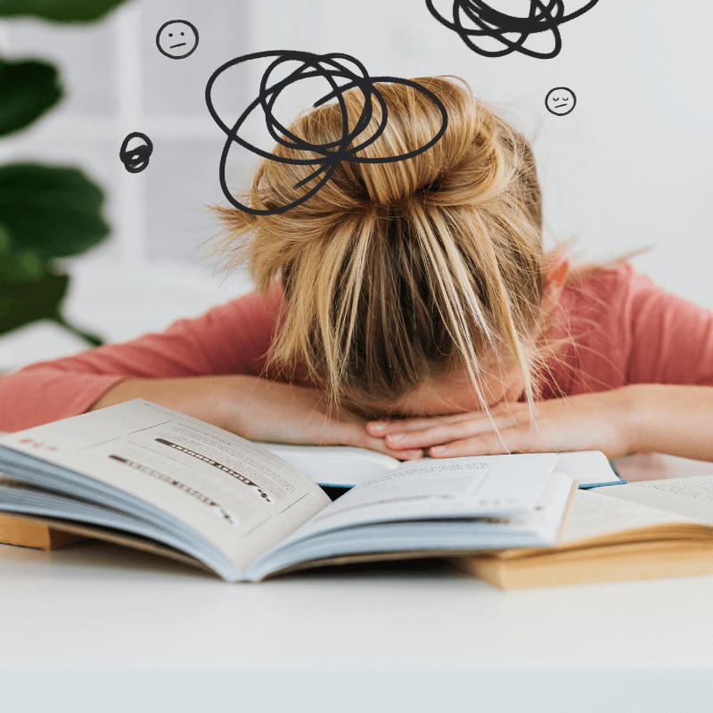 Frau mit Burnout liegt mit dem Kopf auf dem Tisch mit Büchern.
