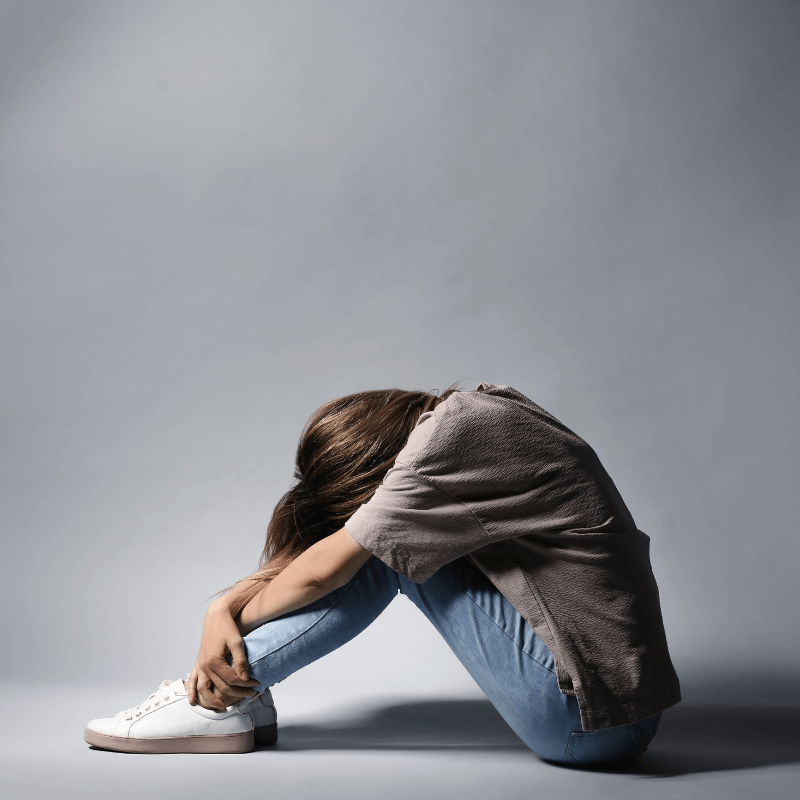 Frau die an einer Depression leidet sitzt mit gesenktem Kopf auf dem Boden.